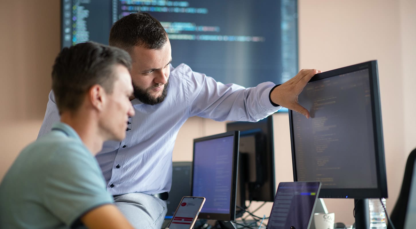Two men collaborating on computers in a modern office setting, focused on their work.